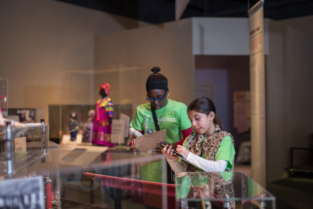 Students take notes in Newcomers - The People of This Place exhibit
